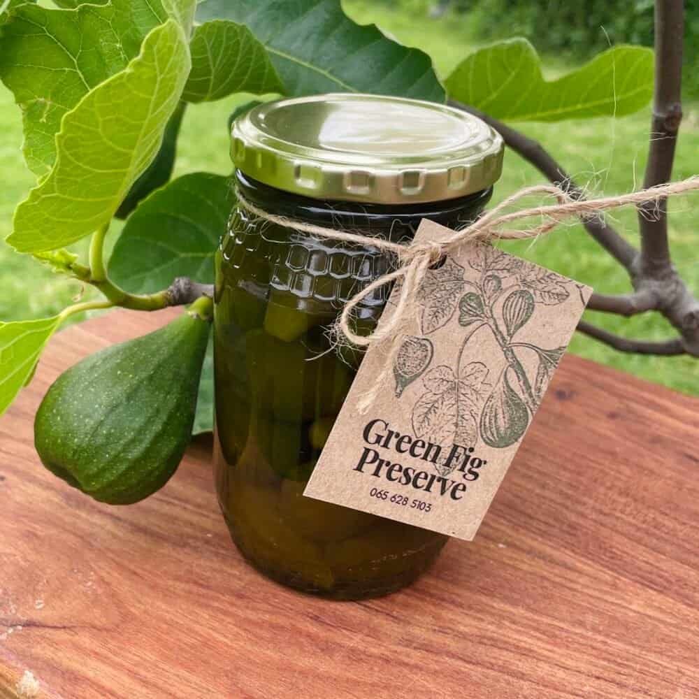 Homemade green fig preserve in a glass jar with a rustic label, perfect for cheese platters.