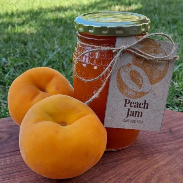 Homemade peach jam in a glass jar with a golden lid, featuring vibrant orange color and a rustic Anita’s Kitchen label, perfect for baked goods and pancakes.